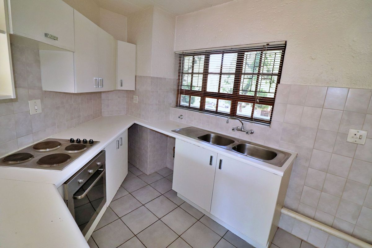 A functional kitchen featuring white built-in cabinetry, laminate countertops, a stainless steel double sink, and integrated electric cooking appliances with tiled finishes.