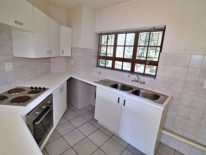A functional kitchen featuring white built-in cabinetry, laminate countertops, a stainless steel double sink, and integrated electric cooking appliances with tiled finishes.