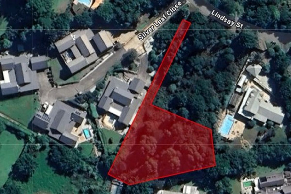 An aerial view highlighting the boundaries of a vacant residential plot surrounded by established trees and neighboring properties.