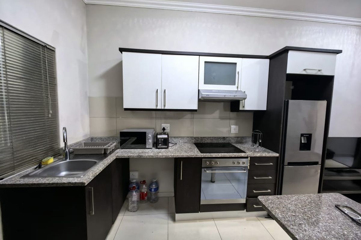 A functional kitchen featuring granite countertops, built-in cabinetry, a stainless steel sink, and integrated cooking appliances including an oven and hob.