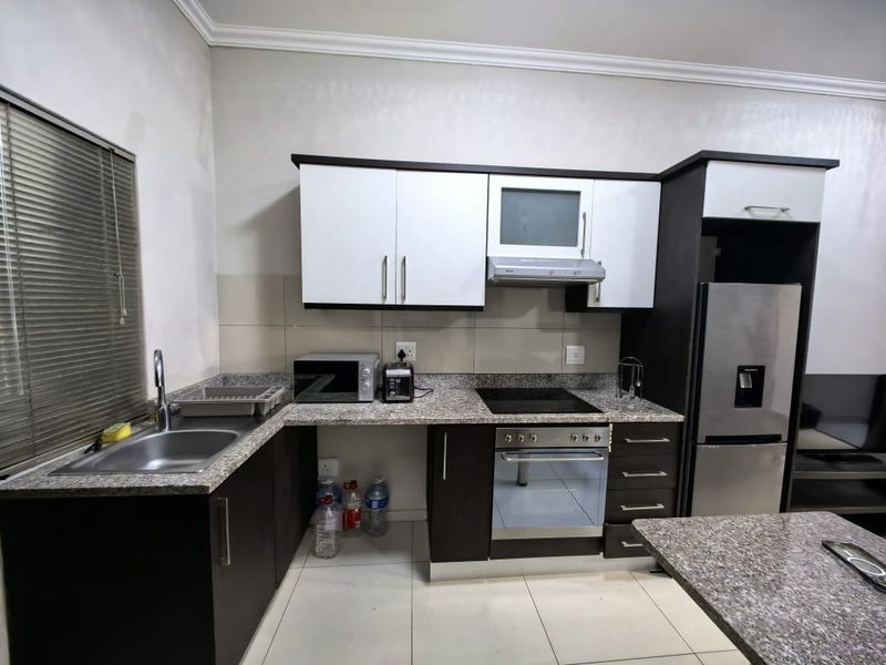 A functional kitchen featuring granite countertops, built-in cabinetry, a stainless steel sink, and integrated cooking appliances including an oven and hob.