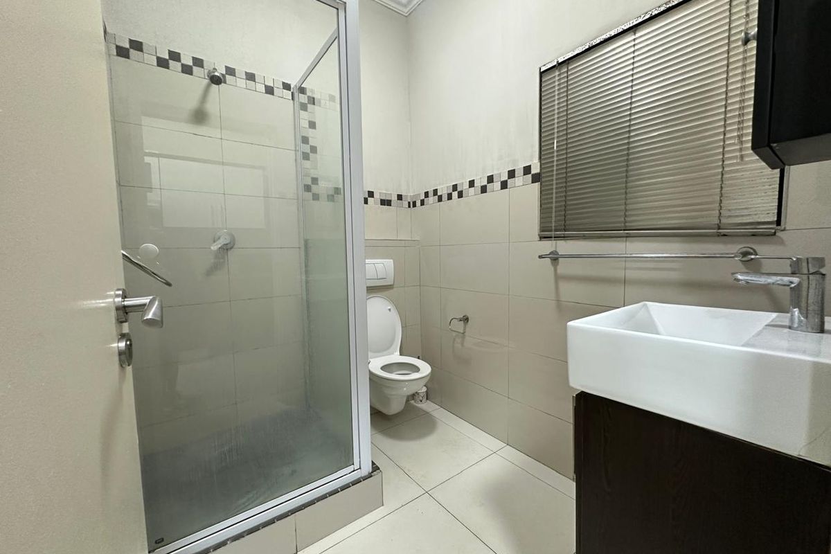 A functional bathroom featuring a glass shower enclosure, wall-mounted toilet, and a modern vanity basin with neutral tiled finishes.