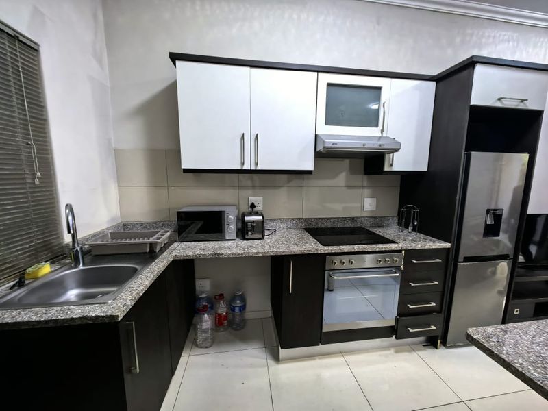 Modern kitchen featuring granite countertops, built-in oven, electric hob, extractor fan, and ample cabinetry, with tiled flooring throughout.