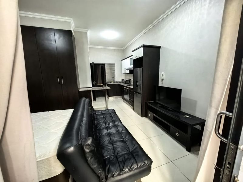 Open-plan apartment living area featuring a compact kitchen with built-in cabinetry, oven, and hob, adjacent to a bedroom area with built-in storage.