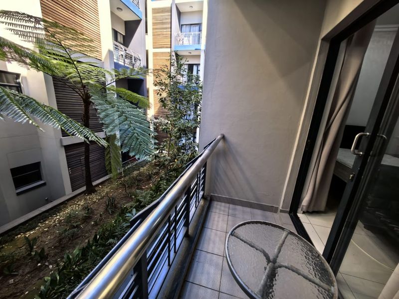 A private balcony featuring tiled flooring and a modern metal balustrade, overlooking a landscaped courtyard area.