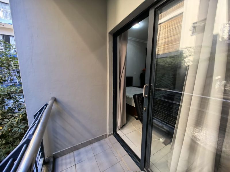 A compact balcony featuring tiled flooring, a metal balustrade, and a large sliding glass door providing access to the interior living space.