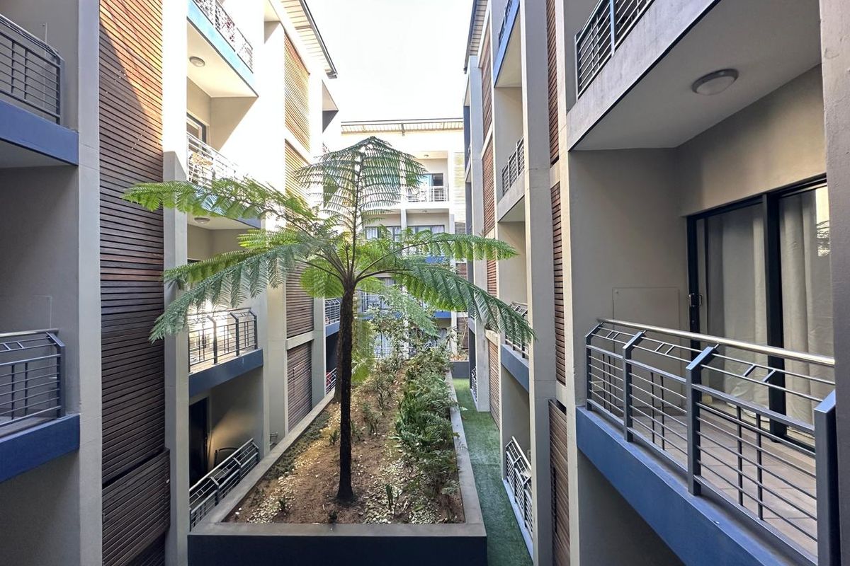 A view of the apartment complex courtyard featuring modern timber cladding, metal balustrades, and a central landscaped garden bed.
