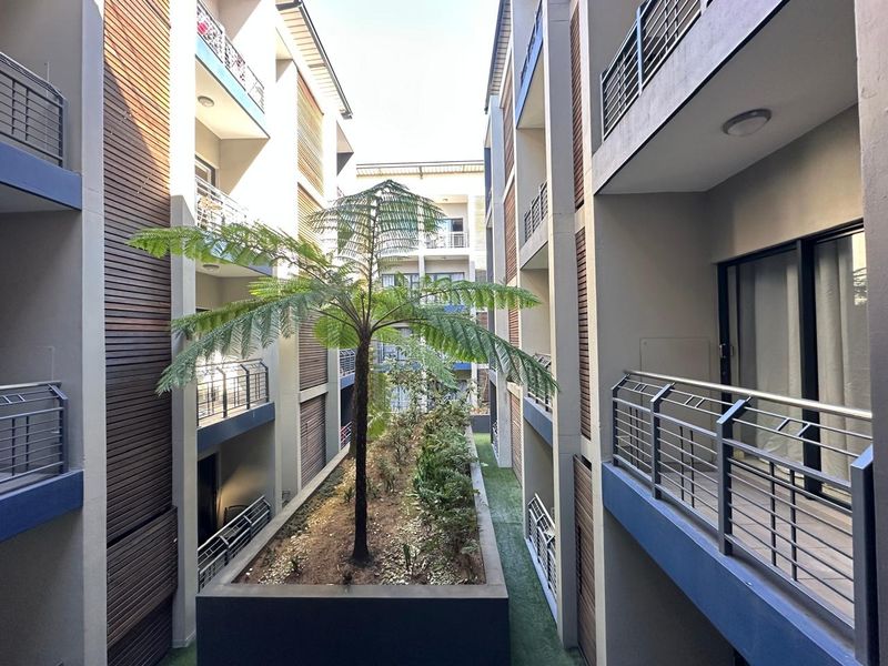A view of the apartment complex courtyard featuring modern timber cladding, metal balustrades, and a central landscaped garden bed.