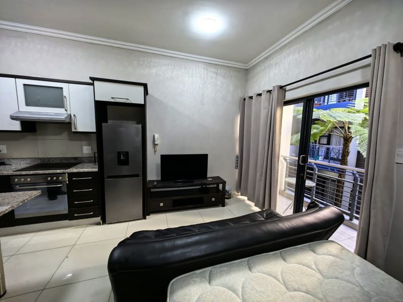 Open-plan living area featuring a modern kitchen with built-in appliances, tiled flooring, and direct access to a private balcony through sliding glass doors.