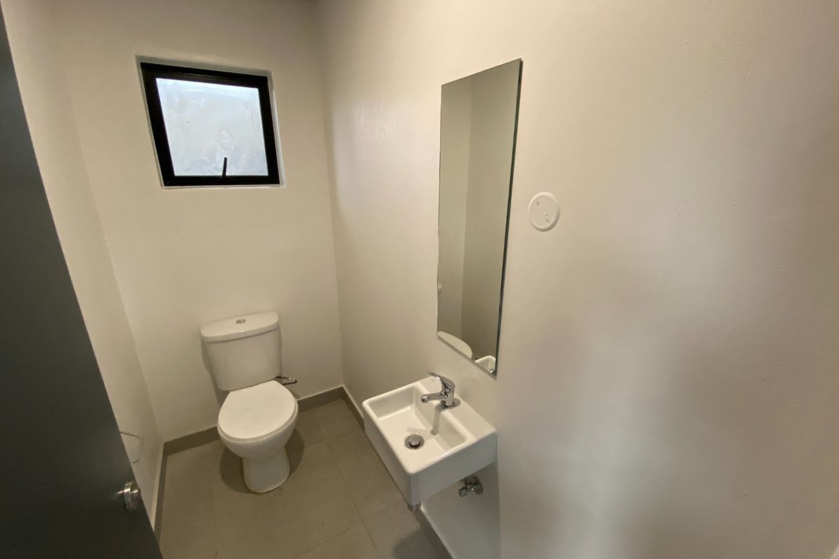 A clean and functional guest bathroom featuring a wall-mounted basin, toilet, and mirror with neutral tiled flooring.