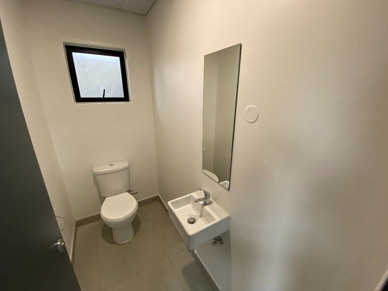 A clean and functional guest bathroom featuring a wall-mounted basin, toilet, and mirror with neutral tiled flooring.