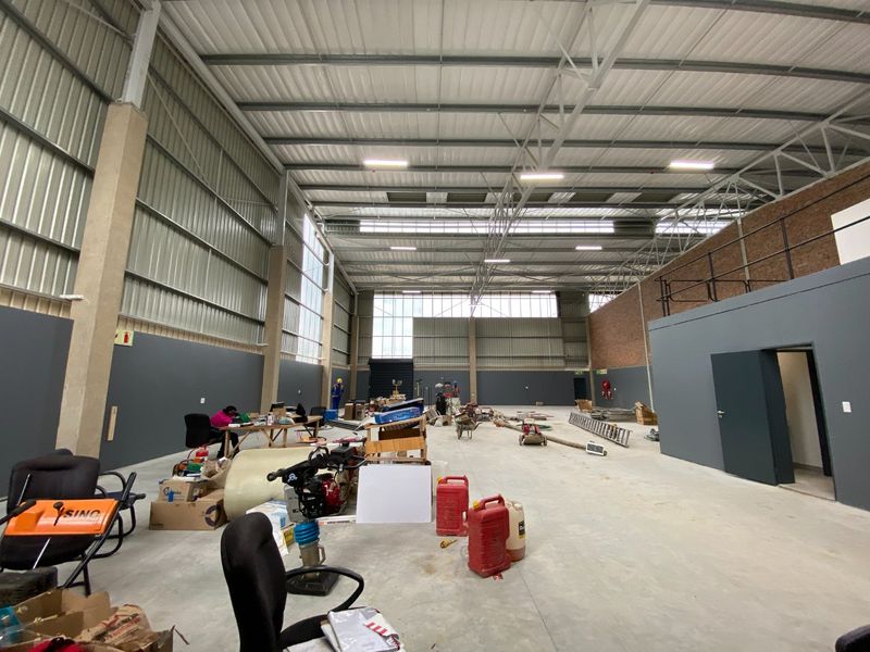 Spacious industrial warehouse unit featuring high ceilings, exposed steel trusses, concrete flooring, and a mezzanine level, suitable for various commercial or storage operations.