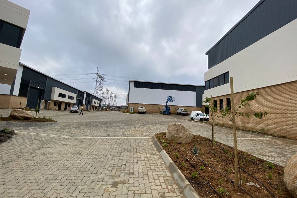 A wide-angle view of a modern industrial park featuring paved driveways, landscaped garden beds, and multiple warehouse units with roller shutter doors.