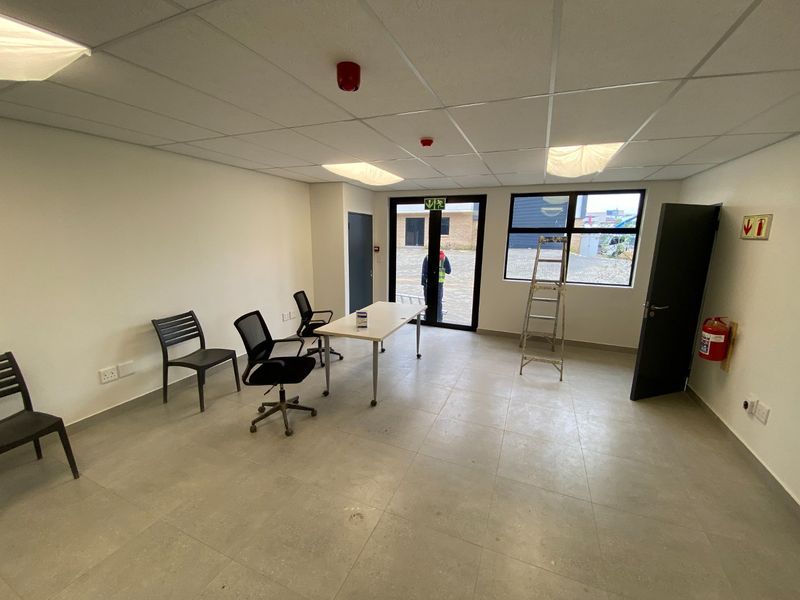 A functional office space featuring a suspended ceiling, tiled flooring, and direct access to the exterior through a glass-panelled door.