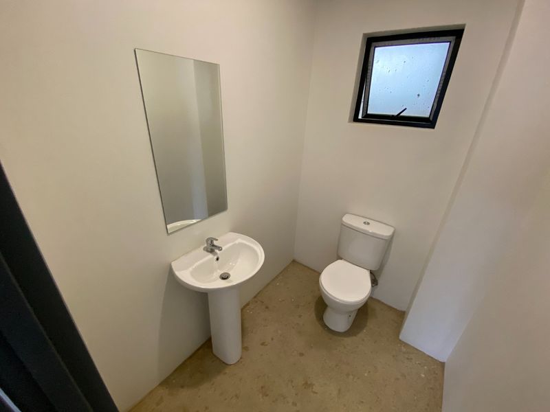 A compact bathroom featuring a pedestal sink, toilet, and wall-mounted mirror, currently awaiting final flooring installation.