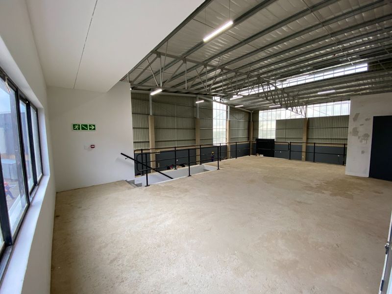 Spacious industrial mezzanine level featuring exposed steel roof trusses, metal cladding, and a functional staircase, offering a versatile open-plan workspace.