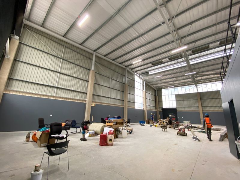 Spacious industrial warehouse unit featuring high ceilings, concrete flooring, and ample natural light through large windows, suitable for storage or manufacturing operations.