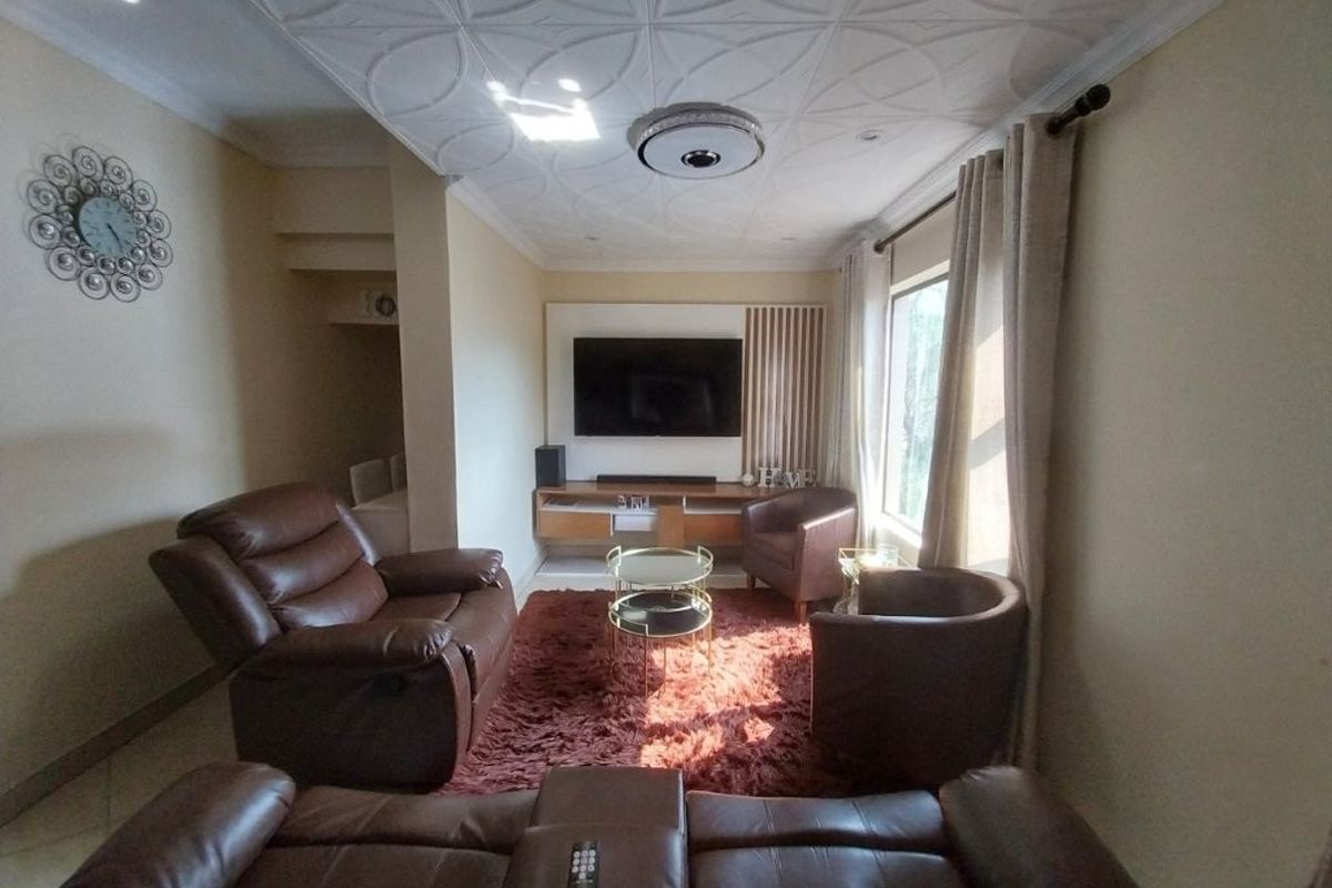 A comfortable living room featuring decorative ceiling detailing, a built-in media console with slatted timber wall accents, and natural light from the side window.