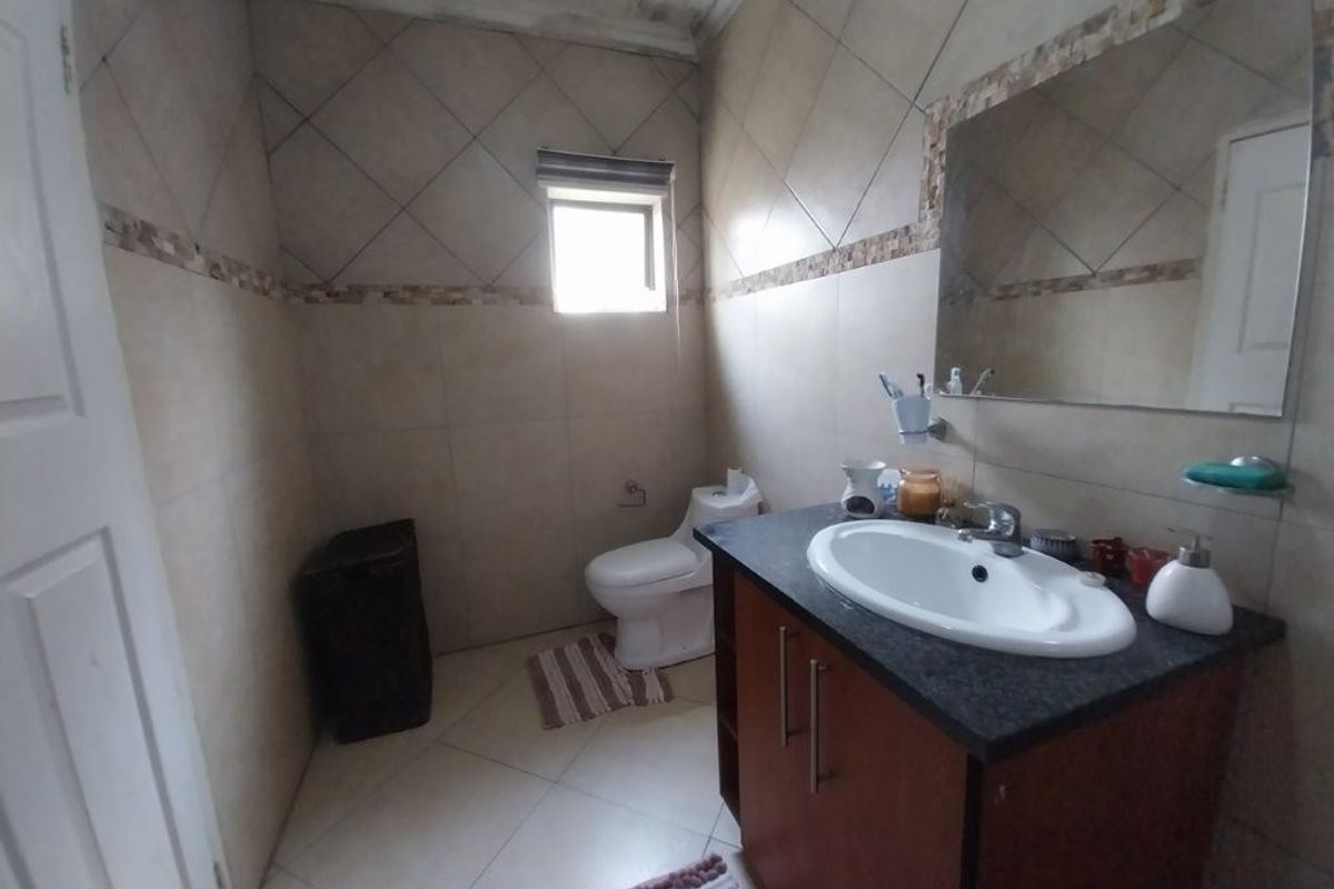 A functional bathroom featuring a vanity cabinet with basin, toilet, and tiled finishes. The ceiling shows signs of wear and requires maintenance.