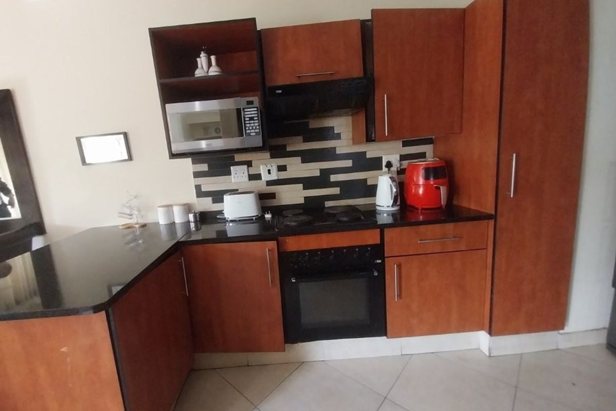 Compact kitchen featuring wood-finish cabinetry, granite countertops, built-in oven, hob, and extractor fan with a modern tiled backsplash.