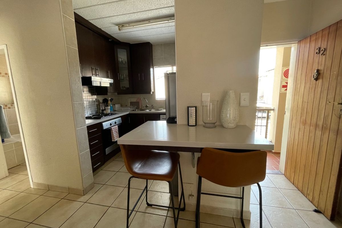Compact kitchen featuring dark wood cabinetry, built-in oven and hob, and a functional breakfast counter, with tiled flooring throughout.