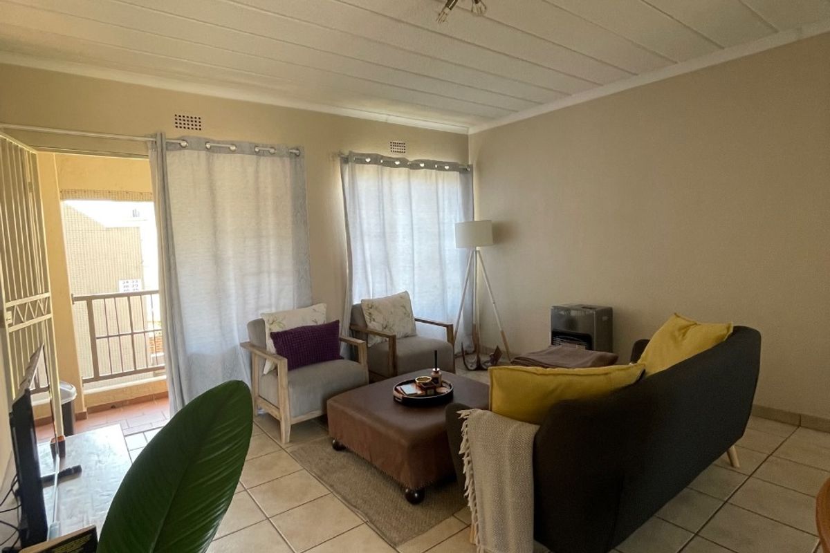 A living room featuring tiled flooring, ceiling panels, and direct access to an outdoor balcony through a security gate and sliding door.