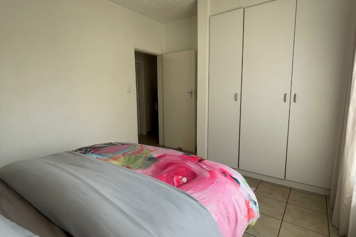 A bedroom featuring built-in cupboards, tiled flooring, and a panelled ceiling, offering a functional space with neutral finishes.