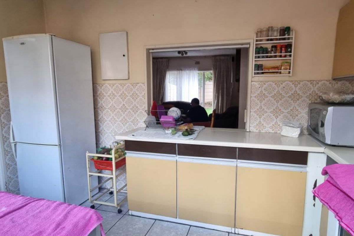 A dated kitchen featuring original cabinetry, laminate countertops, and a convenient pass-through window connecting to the adjacent living area.