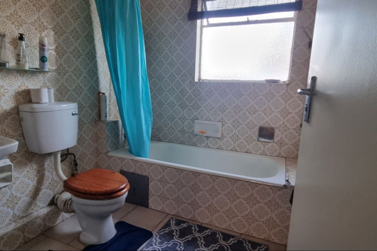 A dated bathroom featuring a pedestal basin, toilet, and bathtub with original patterned wall tiles and a window for natural light.