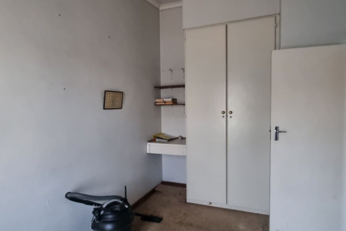 A bedroom featuring a built-in wardrobe, integrated desk, and wall shelving, offering a functional layout ready for modernization.