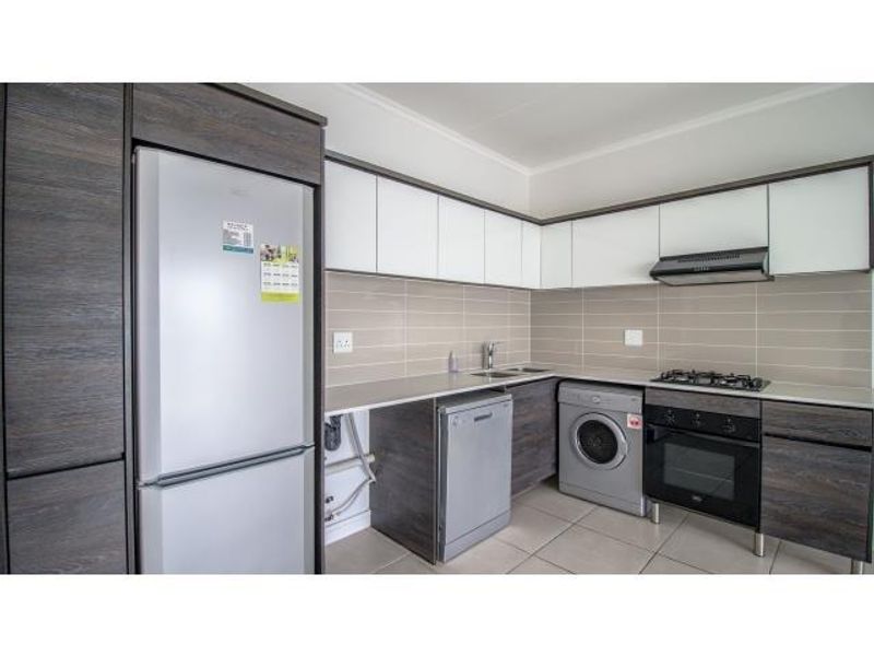 Modern kitchen featuring dark wood and white cabinetry, stone countertops, tiled backsplash, and integrated stainless steel appliances including a gas hob and oven.