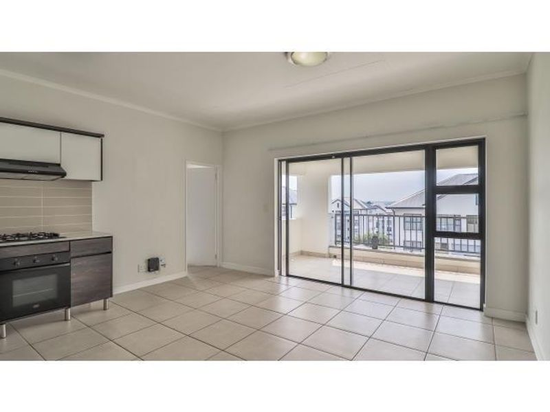 Open-plan living area featuring a modern kitchen with built-in appliances, tiled flooring, and large sliding doors leading to a private balcony.