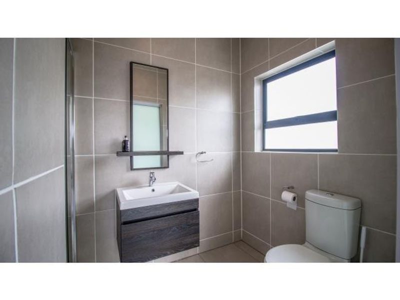 A modern bathroom featuring a wall-mounted vanity with a basin, a shower enclosure, and neutral wall tiling.