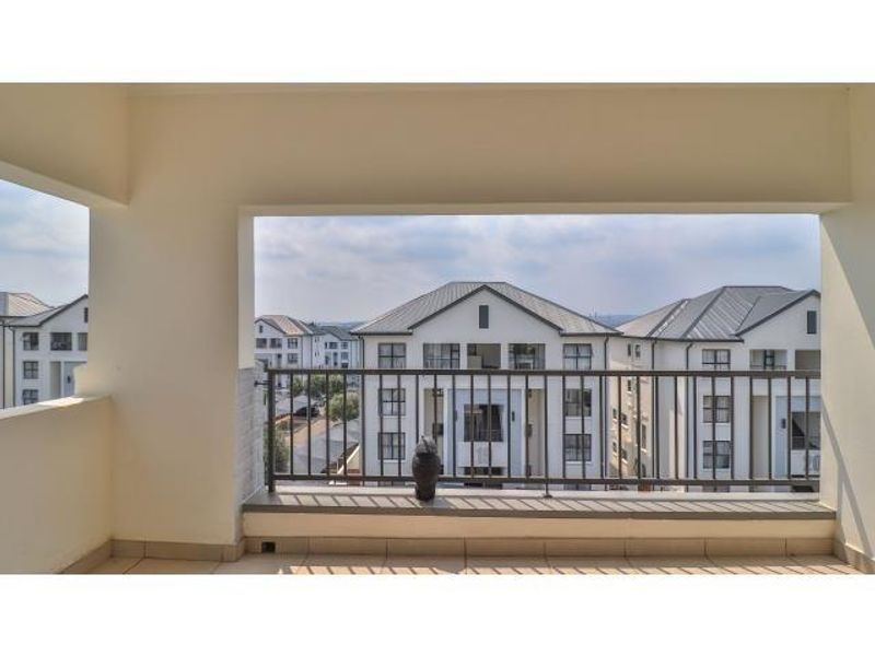 A covered balcony featuring a metal balustrade and tiled flooring, offering an elevated view of the surrounding apartment complex.