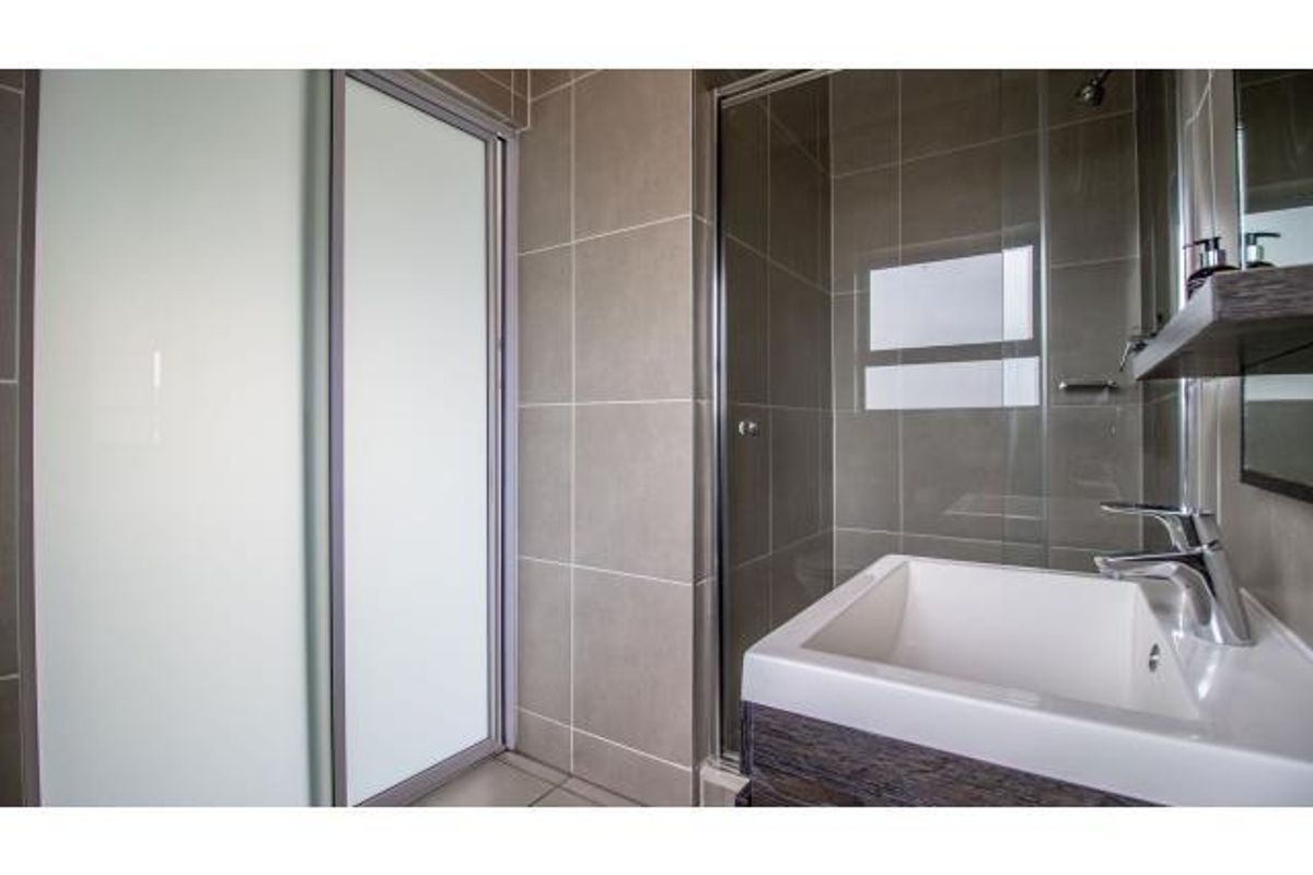 Modern bathroom featuring a glass-enclosed shower, contemporary vanity basin with mixer tap, and neutral wall tiling.