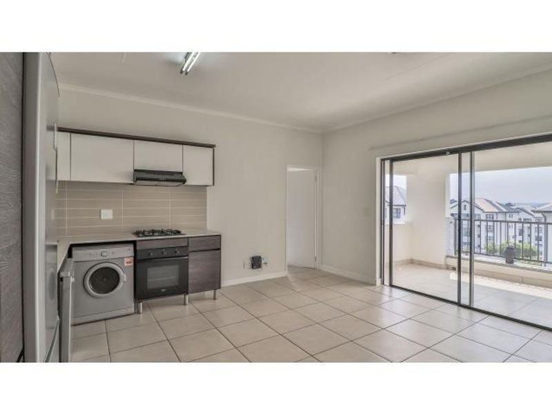 Open-plan kitchen and living area featuring tiled floors, built-in cabinetry with integrated appliances, and direct access to a private balcony.