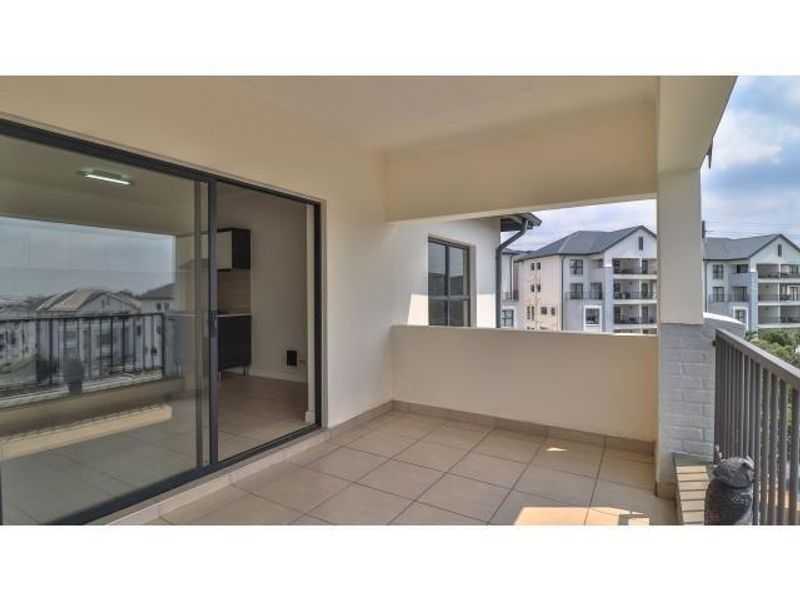 A spacious covered balcony featuring tiled flooring and a metal balustrade, offering a seamless transition from the interior living space.
