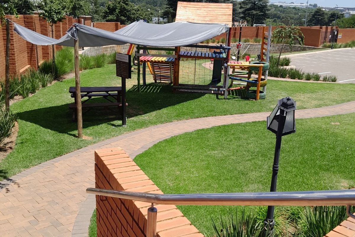 Well-maintained communal garden area featuring a paved walkway, brick retaining walls, stainless steel handrails, and a children's playground structure.