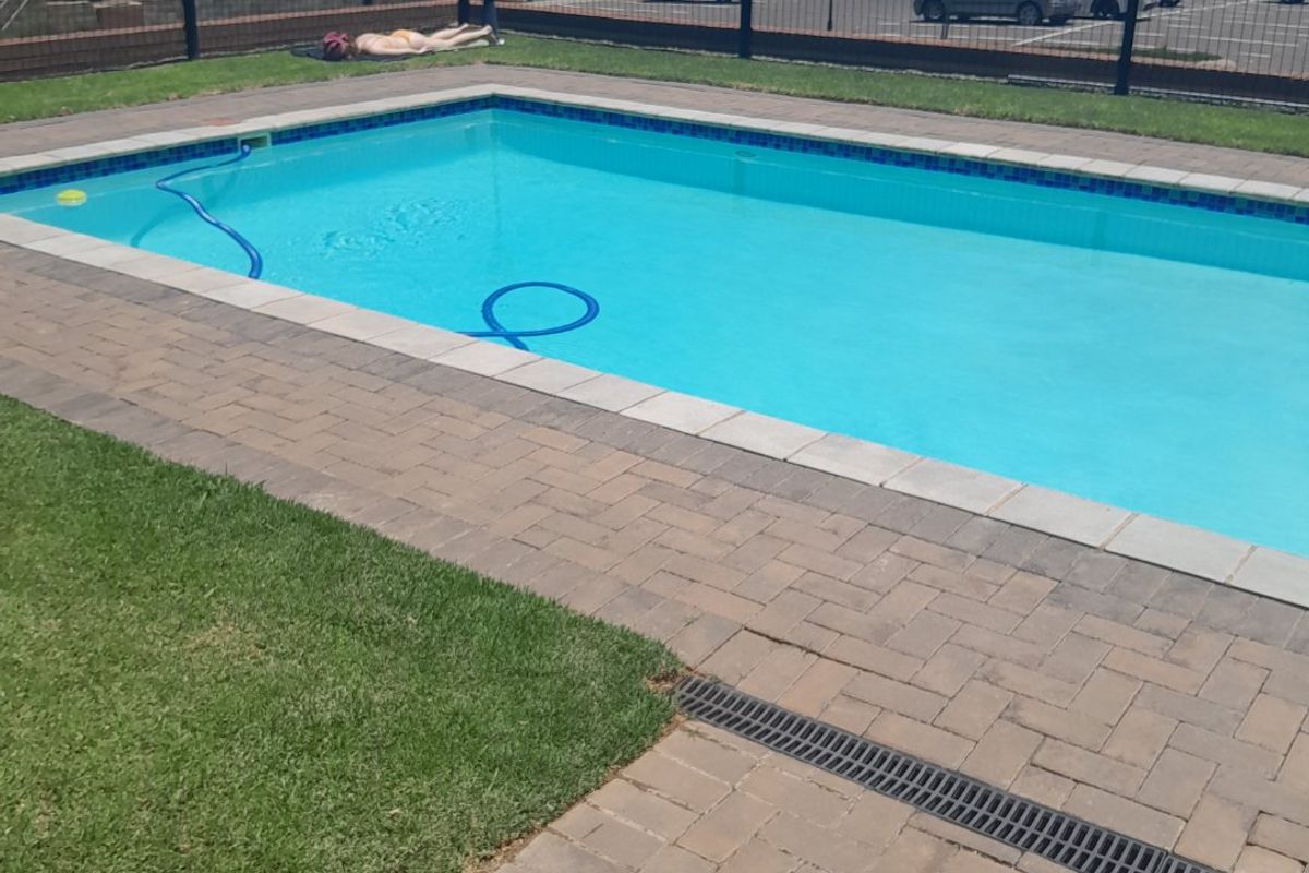 A well-maintained communal swimming pool area featuring paved surrounds, a drainage channel, and a secure perimeter fence.