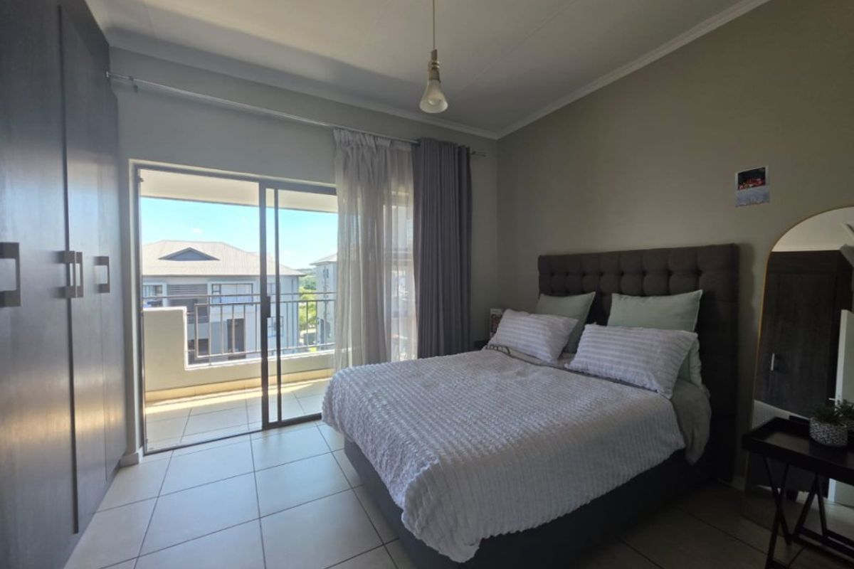 A well-maintained bedroom featuring built-in cupboards, tiled flooring, and a sliding glass door providing direct access to a private balcony.