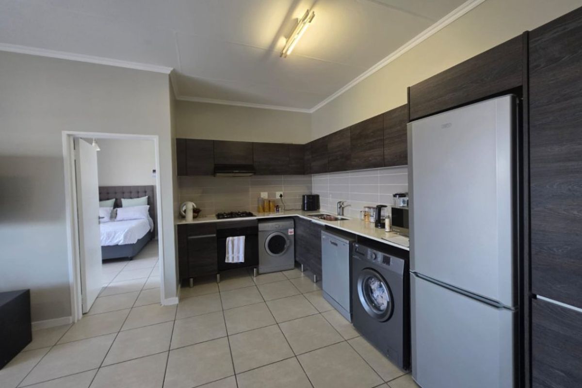 Modern kitchen featuring dark wood-finish cabinetry, light countertops, integrated gas hob, extractor fan, and tiled flooring, with an adjacent bedroom visible.