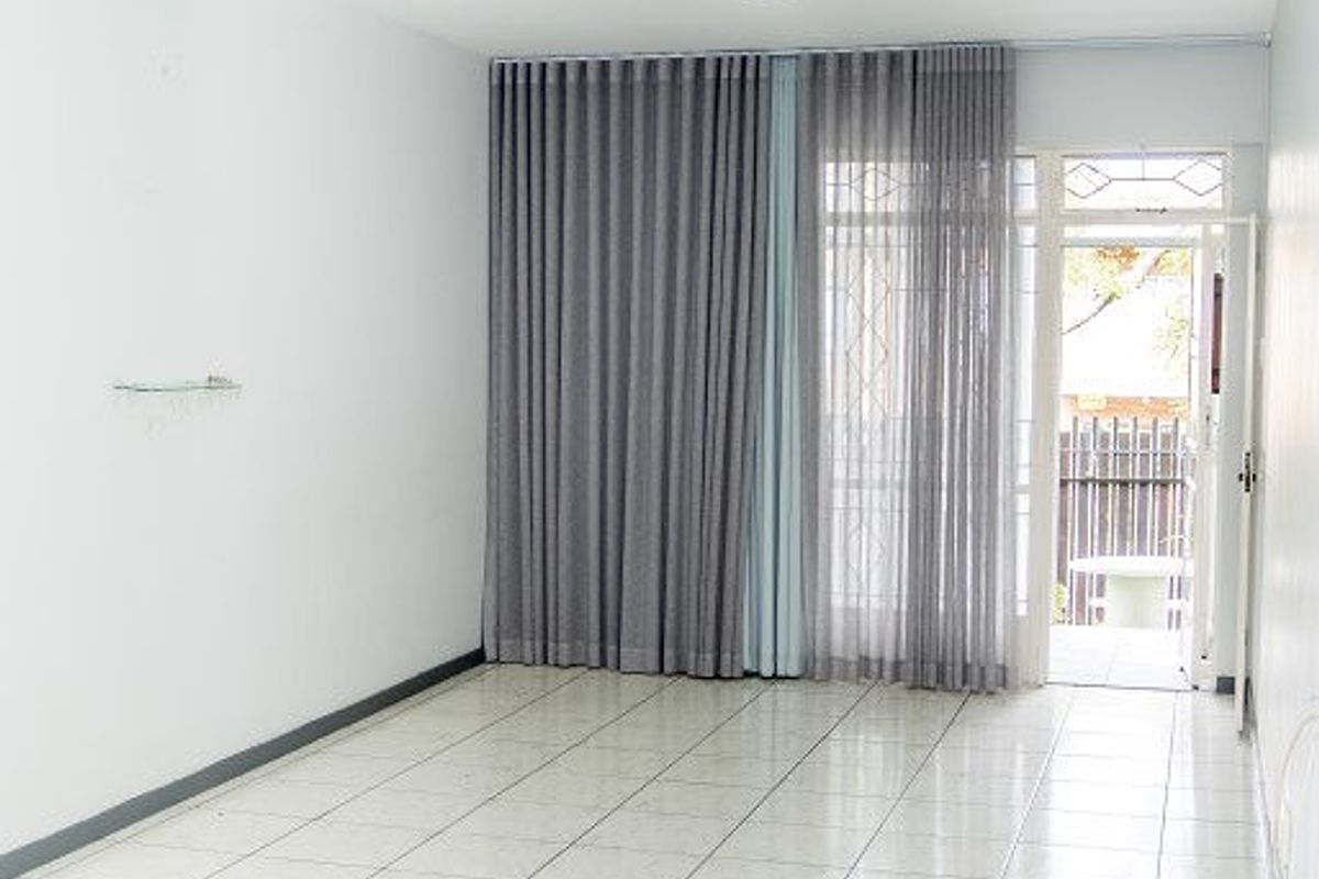 An empty, well-lit living room featuring neutral tiled flooring and a sliding glass door providing access to an outdoor area.