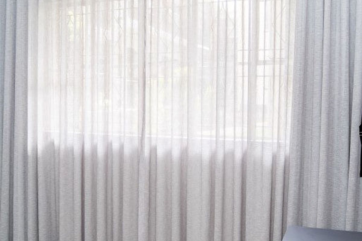 A bright, empty room featuring neutral tiled flooring and floor-to-ceiling curtains covering the window area.