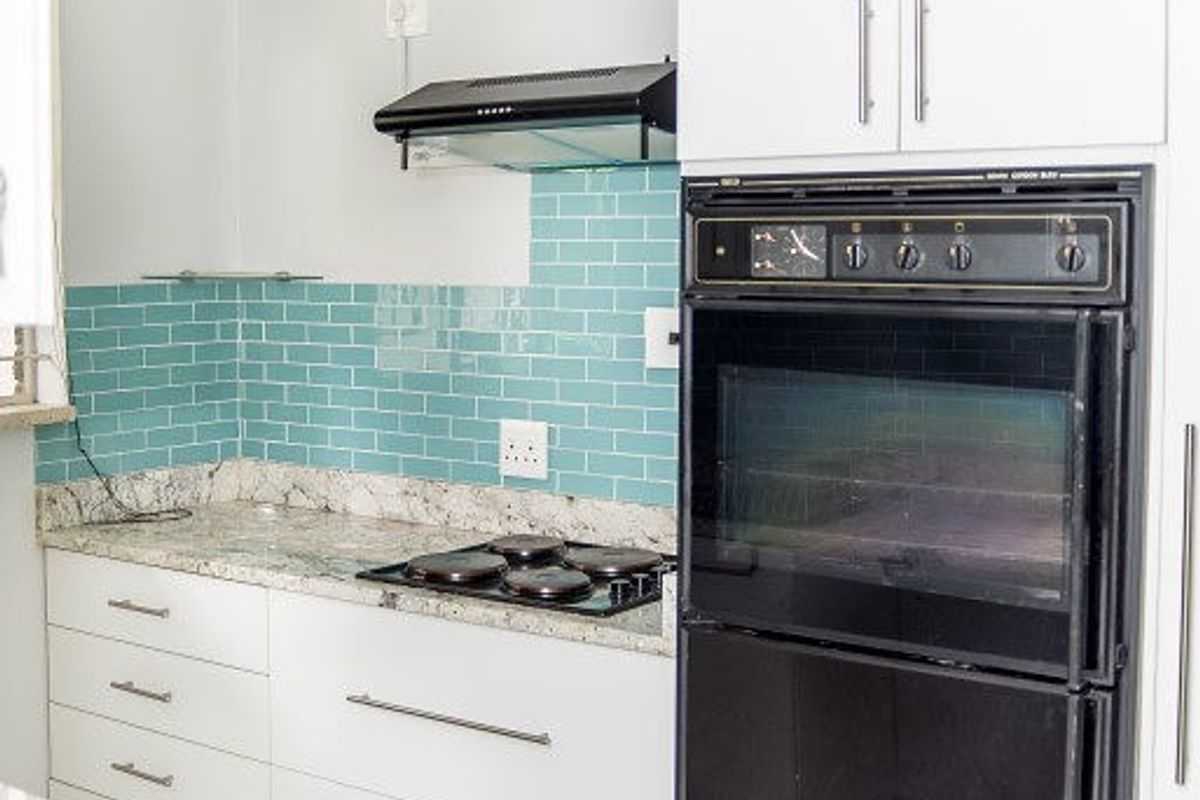 A clean, functional kitchen featuring white cabinetry, granite countertops, a subway tile backsplash, and built-in oven and hob appliances.