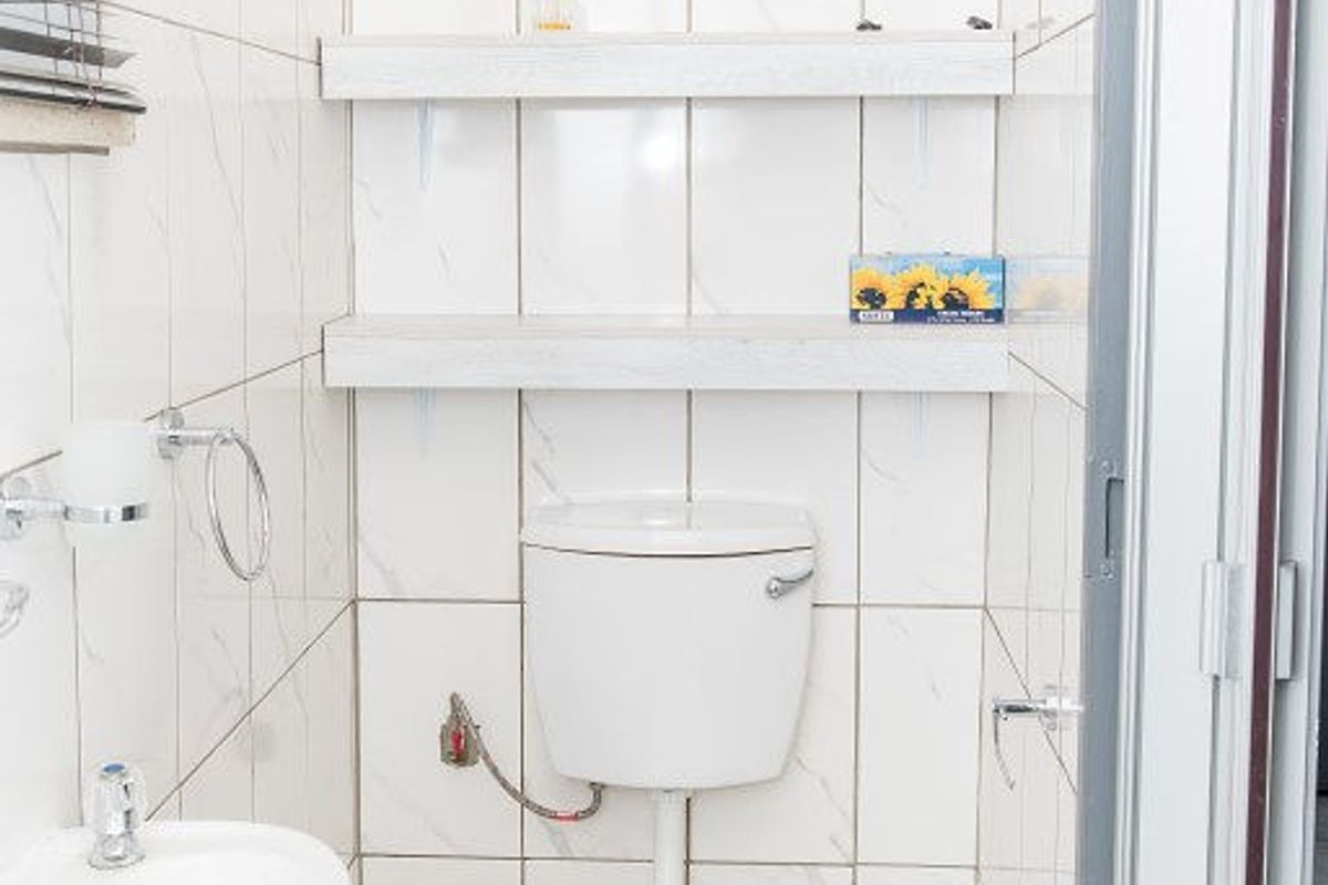 Compact bathroom featuring white ceramic wall and floor tiles, a standard toilet, pedestal basin, and convenient floating shelving for storage.