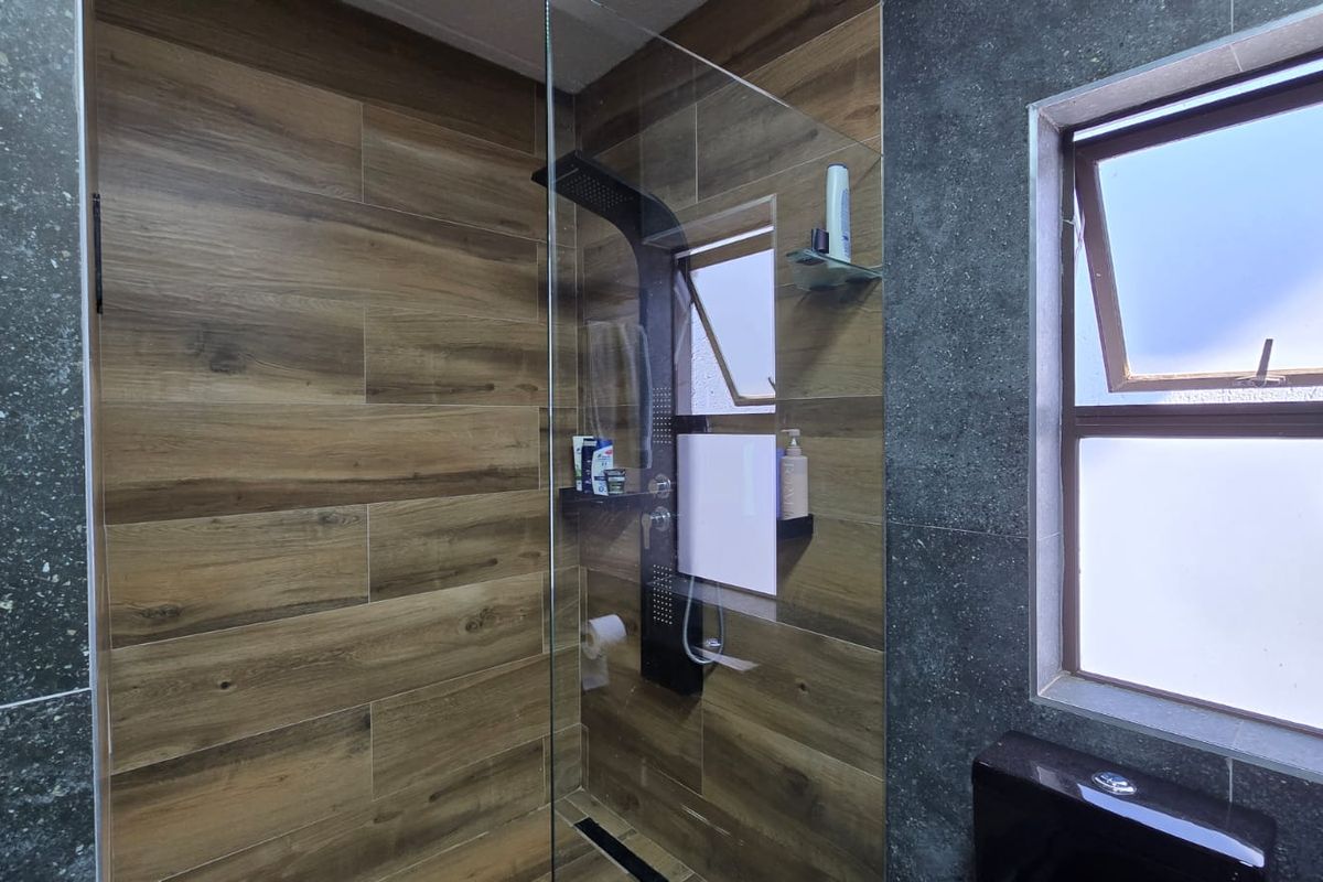 Modern bathroom featuring a walk-in shower with a black panel, glass screen, and a combination of wood-look and dark stone-look wall tiling.