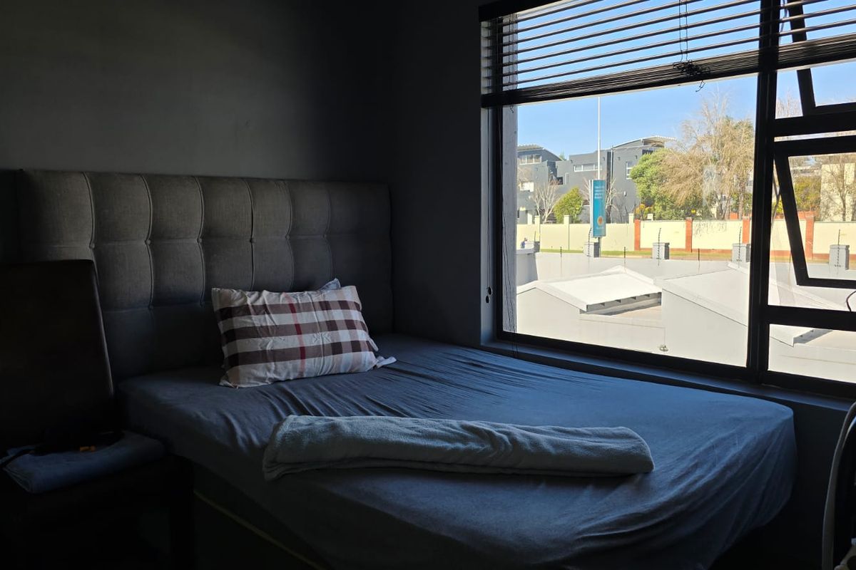 A bedroom featuring dark walls and a large window with venetian blinds, offering natural light and an exterior view.