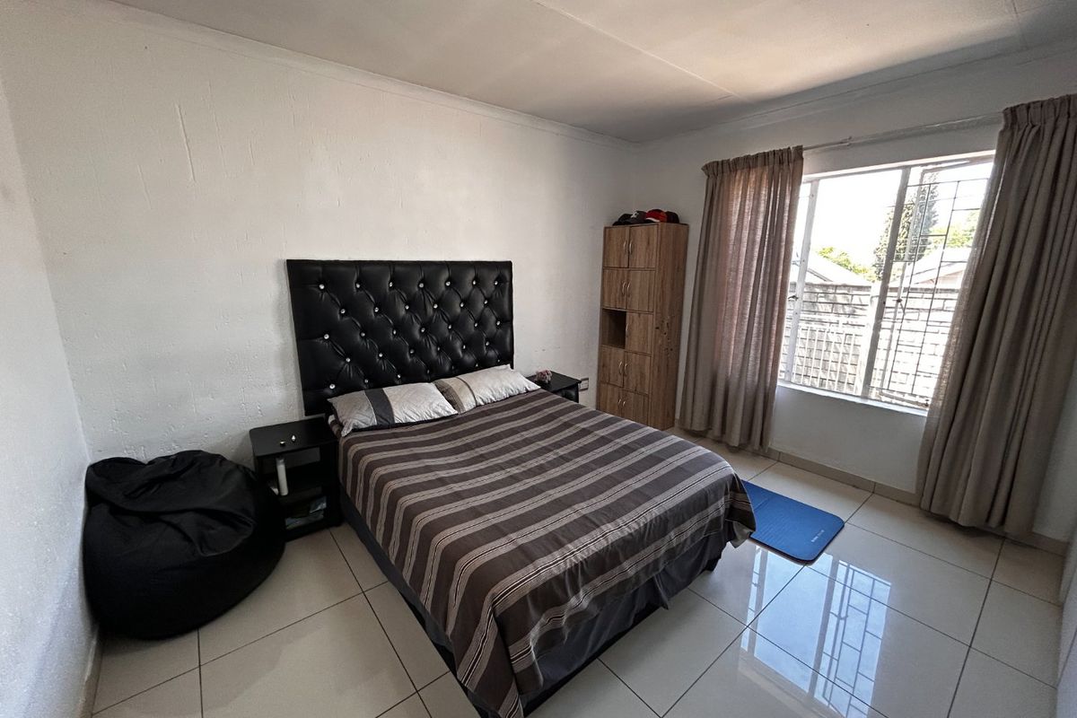 A bedroom featuring tiled flooring, a window with security bars, and neutral wall finishes.