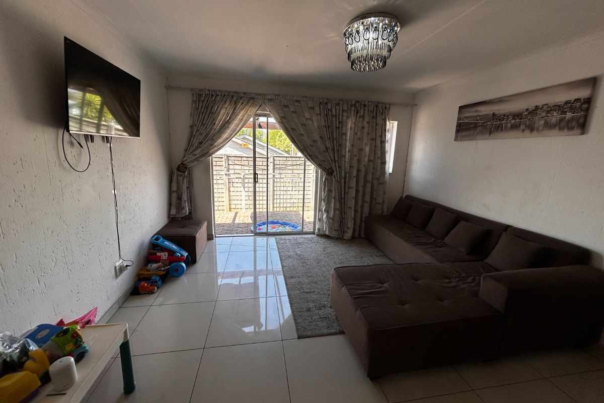 A living room featuring tiled flooring, a crystal chandelier, and a sliding glass door providing access to an outdoor patio area.