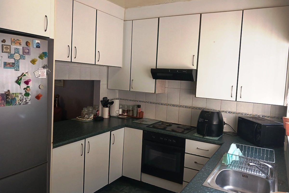 A functional kitchen featuring white cabinetry, dark laminate countertops, a built-in oven with hob, and a stainless steel sink.